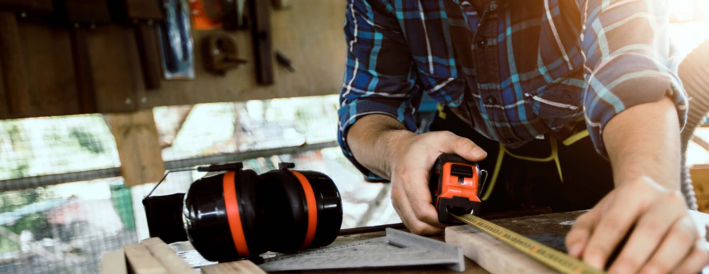 Ein Tischler misst ein Stück Holz aus.