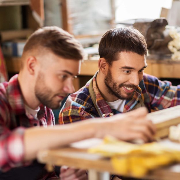 Zwei Handwerker arbeiten gemeinsam in einer Werkstatt und konzentrieren sich auf ein Holzprojekt, während sie hochwertigen handwerklichen Service bieten.