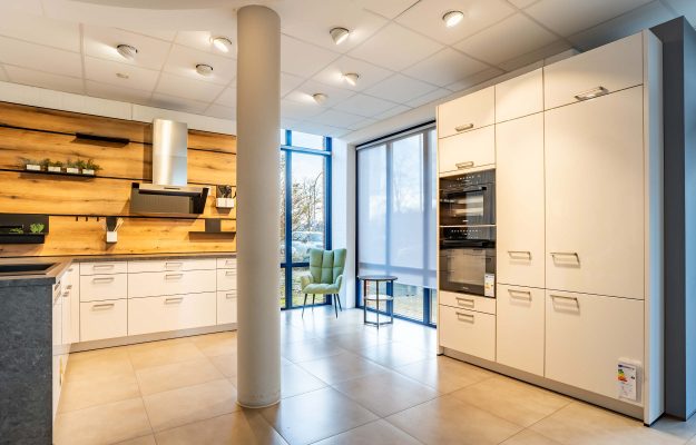 Weiße L-Küche, klassisch mit grauer Steinarbeitsplatte und Holznischenrückwand im Küchenstudio in Langwedel.