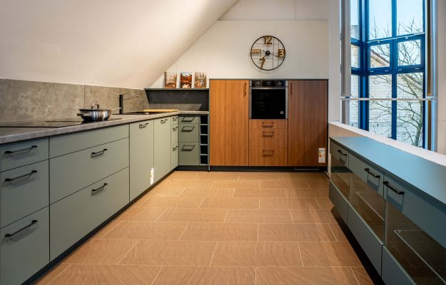 U-Küche in grau-blau mit Steinarbeitsplatte und Steinnischenrückwand mit einem Holzschrank als Highlight.