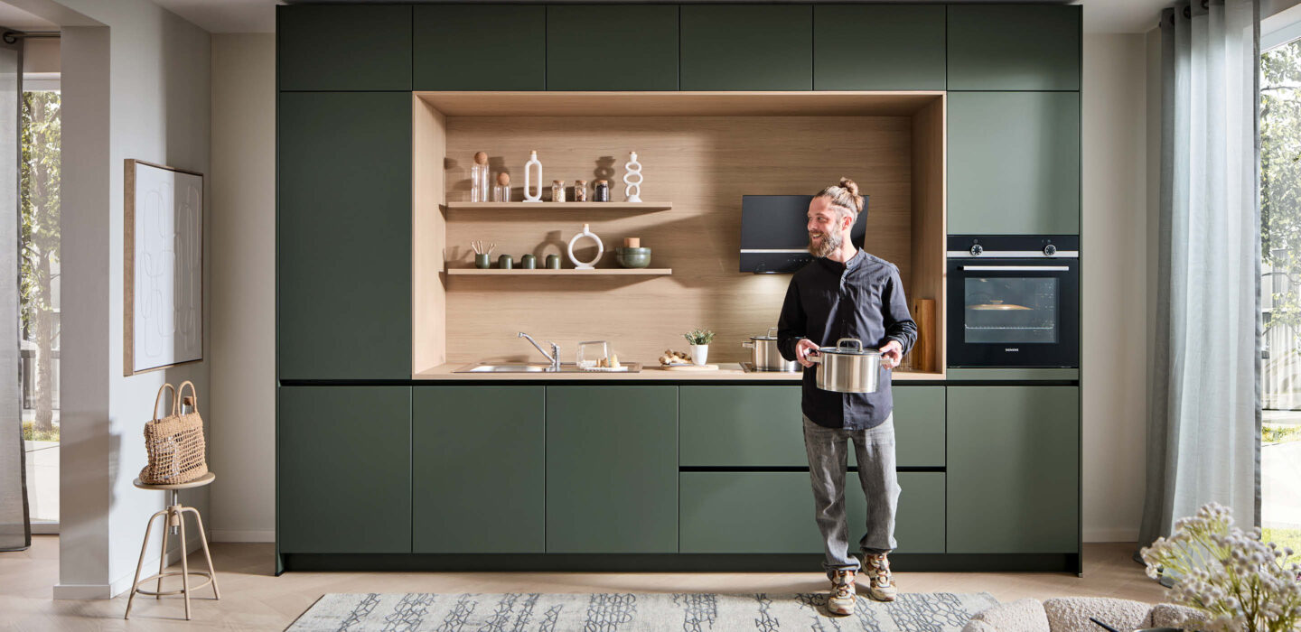 Moderne Küche mit matten grünen Fronten und offenen Holzregalen – harmonische Kombination aus Natürlichkeit und Funktionalität.