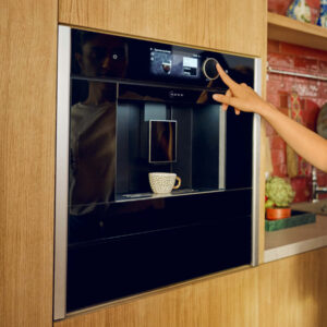 Neff Einbau-Kaffeevollautomat mit Touchdisplay und Drehregler, integriert in Holzküche, bereitet Espresso in Tasse im modernen Küchenumfeld