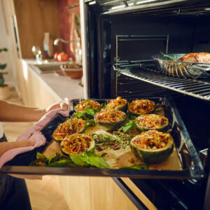 Neff Backofen mit geöffneter Tür und Backblech mit gefülltem Gemüse, moderne Einbauküche, Zubereitung von Speisen im warmen Küchenambiente