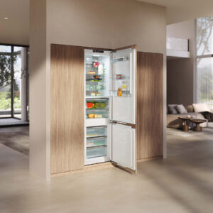Miele Einbaukühlschrank mit Gefrierfach hinter Holzfront, geöffnet und gefüllt mit Lebensmitteln, integriert in moderne, helle Wohnküche