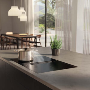 Miele Induktionskochfeld mit integriertem Dunstabzug auf moderner Kücheninsel aus Stein, mit Topf und Dampfentwicklung im hellen Wohnraum