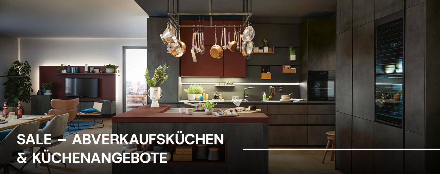 Sale für Abverkaufsküchen und Küchenangebote: moderne offene Wohnküche mit großer Kücheninsel, dunklen grifflosen Küchenmöbeln, rotbraunen Akzenten und integrierten Einbaugeräten.
