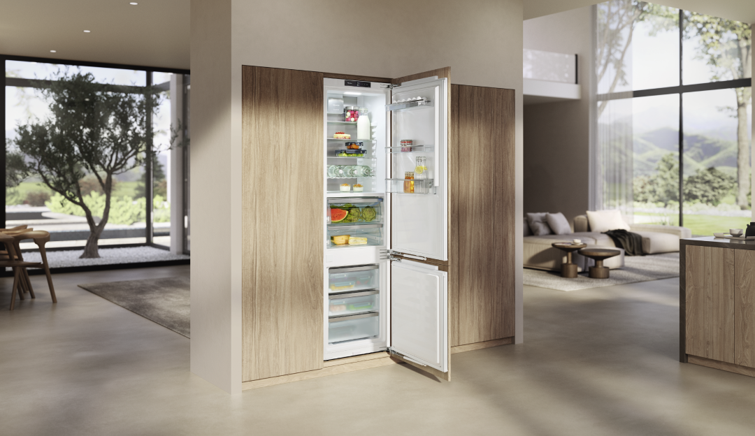 Integrierter Kühl- und Gefrierschrank in moderner Küche mit Holzfronten – geöffnete Kühl-Gefrierkombination mit übersichtlich gelagerten Lebensmitteln bei Helmke Küchen.