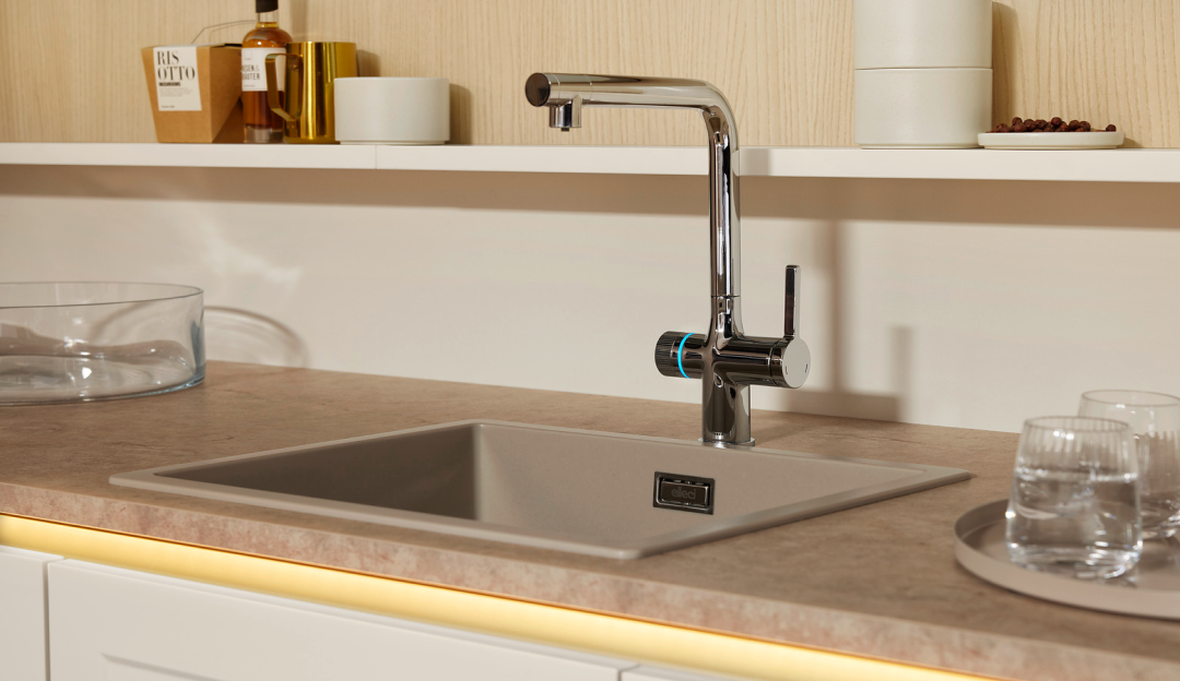 Moderne Küchenspüle mit hochwertiger verchromter Armatur, heller Arbeitsplatte und indirekter Beleuchtung – funktionale Ausstattung und modernes Küchendesign bei Helmke Küchen.