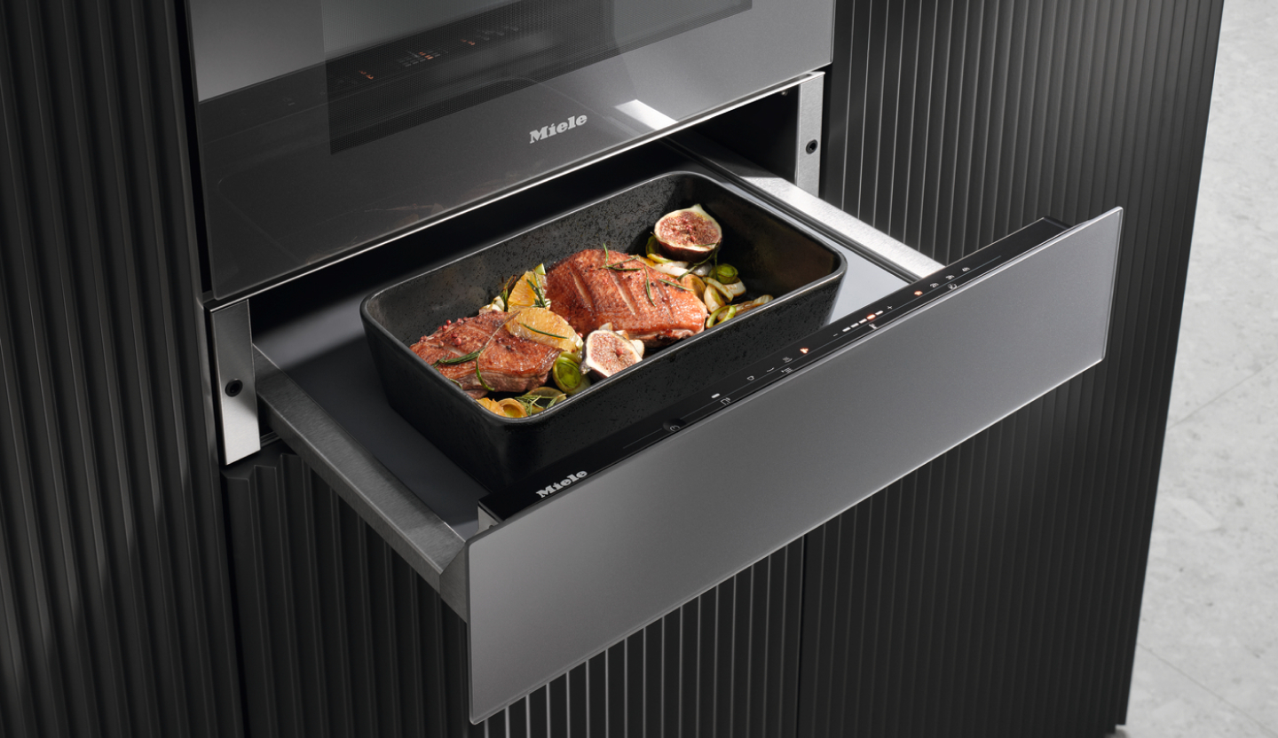 Geöffnete Miele-Einbauschublade mit einem Bräter und zubereiteten Speisen unter dem Backofen.